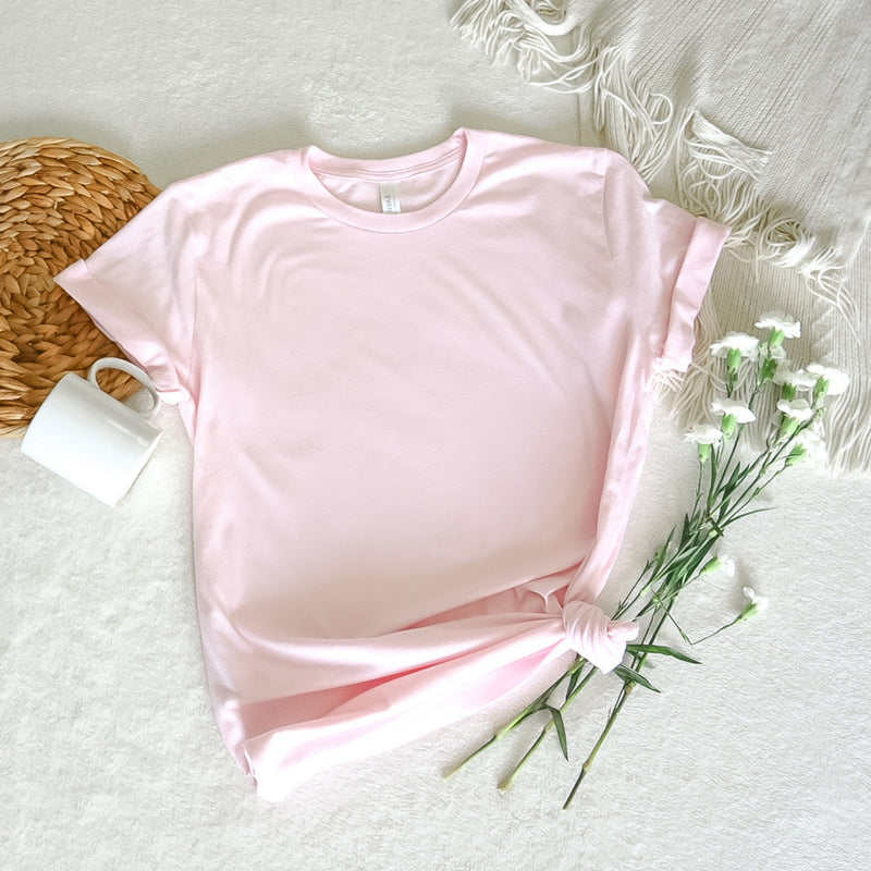 a pink t - shirt and some flowers on a white blanket